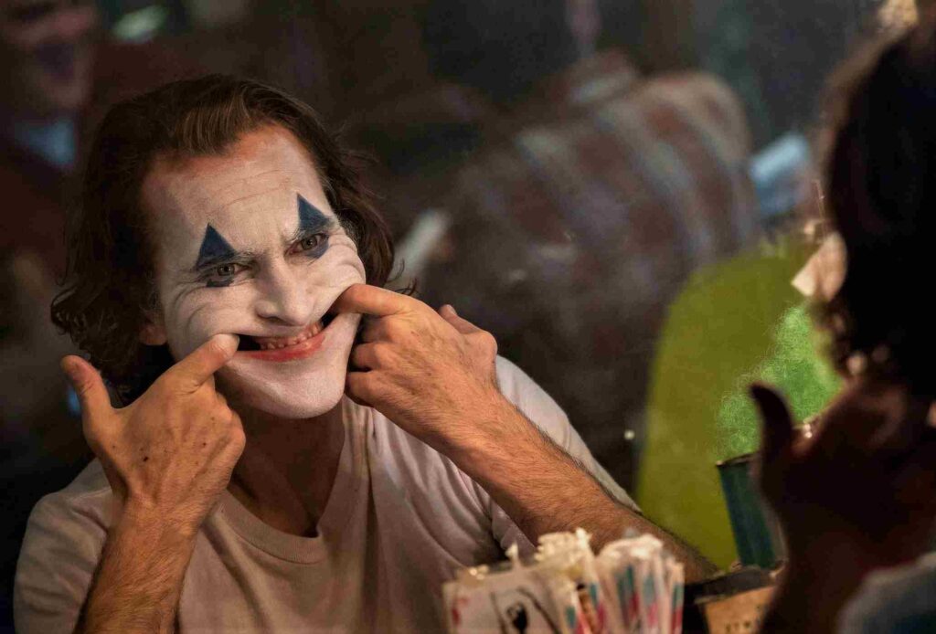 Joaquin Phoenix pulling his lips with his fingers for fake smile as Joker.