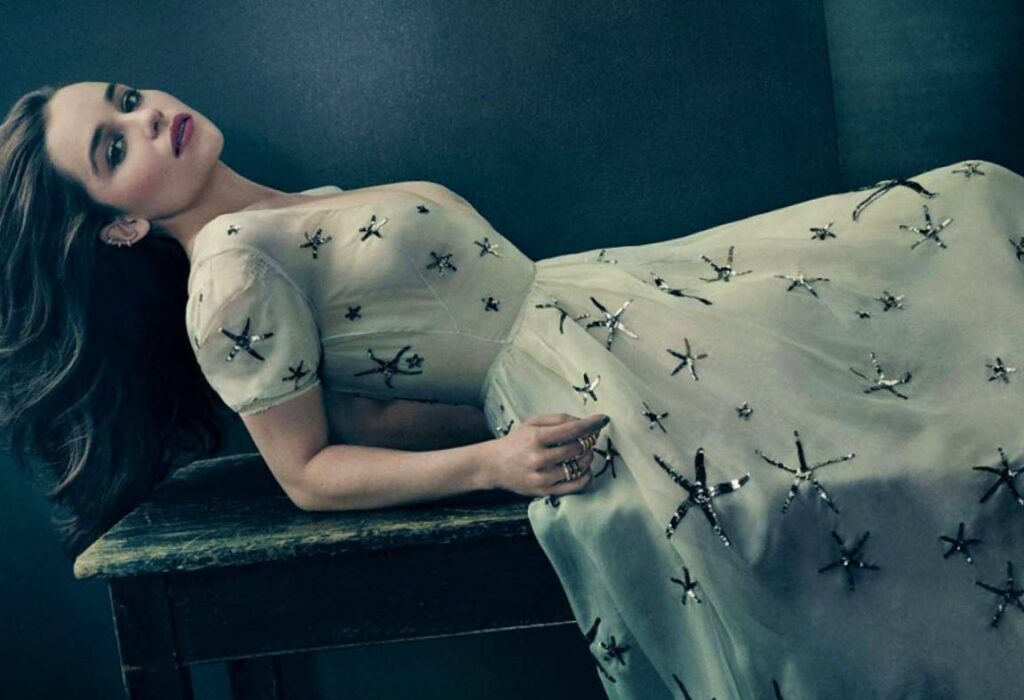 Emilia Clarke looking hot and gorgeous while lying on a table in a white dress.